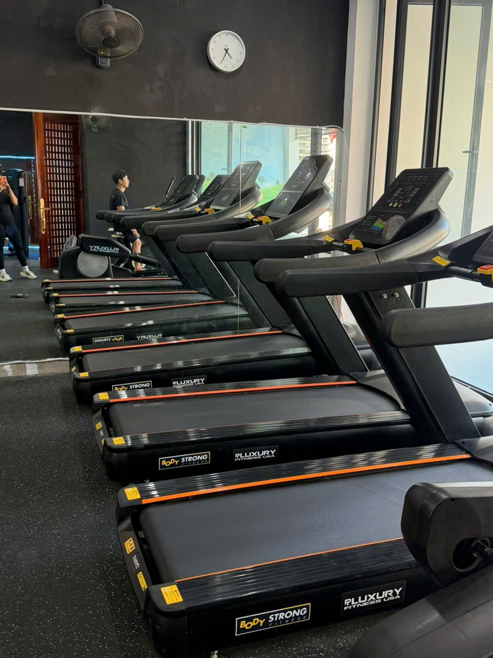 Khu cardio ngoài trời tầng 1 với dãy máy chạy bộ, xe đạp tập và máy elliptical bên cửa kính lớn